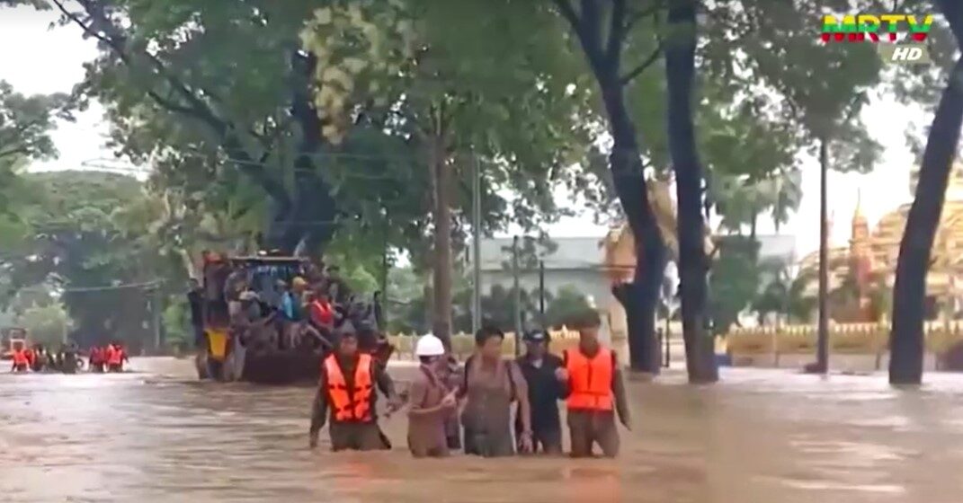 people wade through flood water in Myanmar