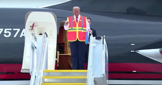 Trump walks down plane stairs wearing a bright construction vest