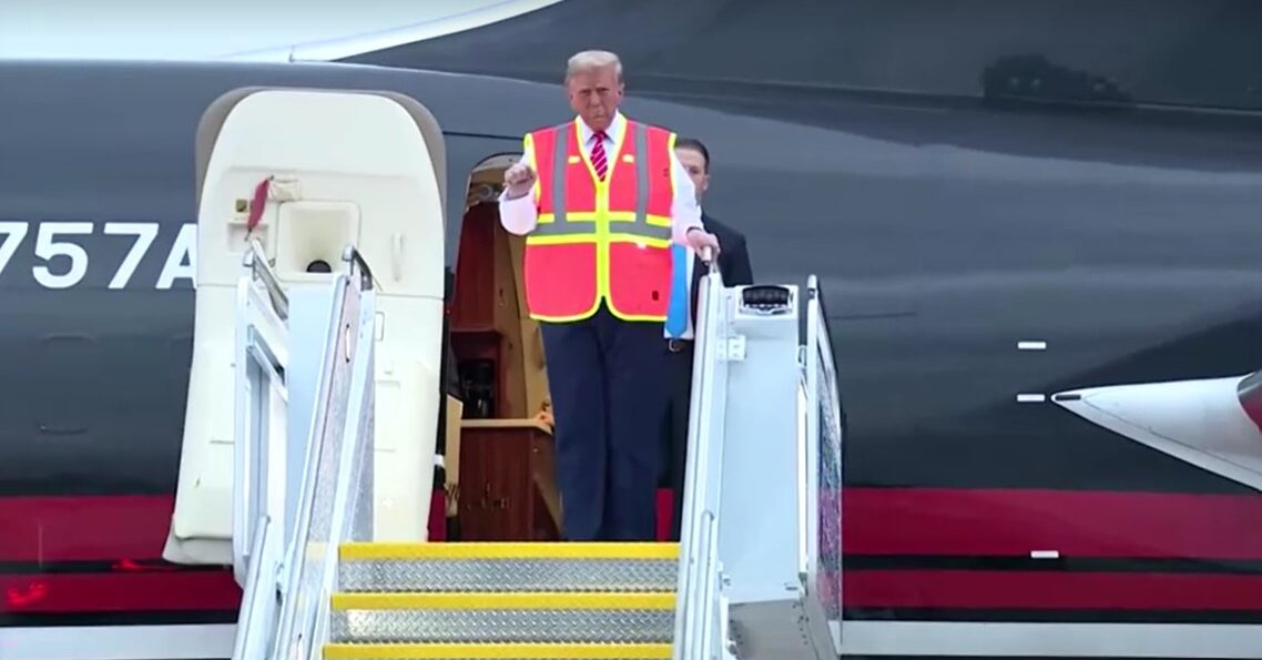 Trump walks down plane stairs wearing a bright construction vest